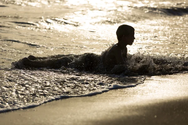 Jonge jongen legt in water aan het zandstrand, zonsondergang — Stockfoto