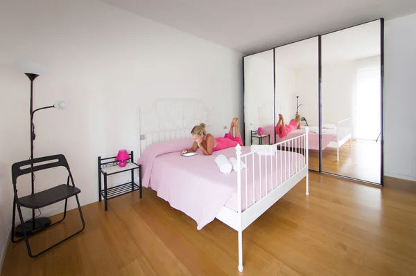 Interno della stanza bianca, donna bionda vestita rosa sul letto — Foto Stock