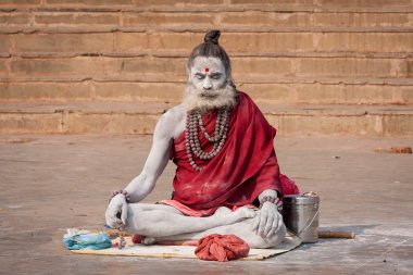 Hindu sadhu holy man, sits on the ghat near the Ganges river in Varanasi, India clipart