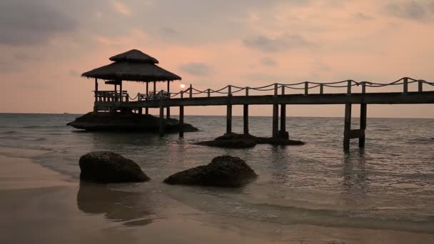 Spiaggia di sabbia tropicale con molo vicino all'acqua di mare al tramonto — Video Stock