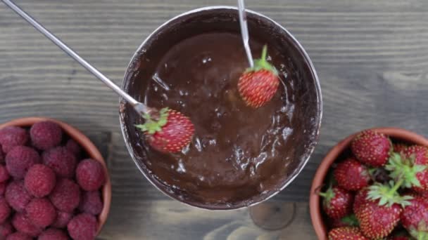 Children takes the red strawberries on a fork dunks in hot chocolate from the fondue — Stock Video
