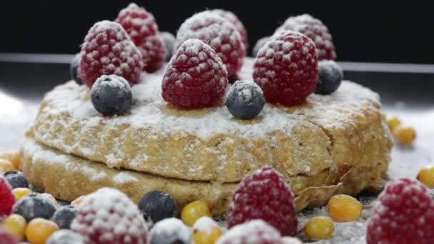 Cake with raspberries, blueberries, sea buckthorn sprinkled with powdered sugar on a black plate rotates — Stock Video