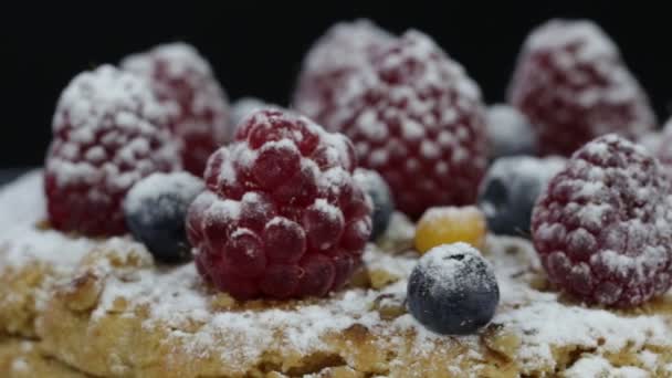 Tårta med hallon, blåbär, havtorn beströdda med florsocker på en svart platta roterar — Stockvideo