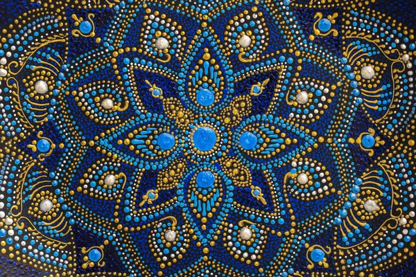 Decorative ceramic plate with black, blue and golden colors, painted plate on background, closeup, top view. Decorative porcelain plate painted with acrylic paints, handwork, dot painting
