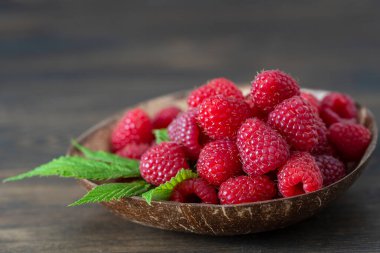 Kahverengi ahşap arka planda, hindistan cevizi tabağında kırmızı ahududu hasadı. Kapat.