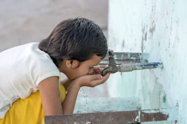 RISHIKESH, INDIA - 06, 2018: Hintli susamış bir kızın portresi Rishikesh, Hindistan 'da sokak musluğundan su içiyor