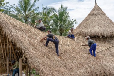 UBUD, BALI, INDONEZYA - 24 Mart 2019: Yerel halk Ubud, Bali, Endonezya 'da yeni bir saman çatısını onarıyor. İnşaat işçileri binanın çatısında çalışıyor.