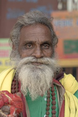 RISHIKESH, INDIA - NOVEMBER 06, 2018: Hindu sadhu kutsal adam portresi, ghat üzerinde oturuyor ve Hindistan 'ın Rishikesh kentindeki Ganj nehrinin yakınındaki yoldan geçenlerden sadaka istiyor.