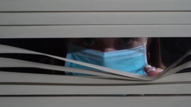 İçerideki koruyucu maskeli genç kızın ön portresini kapat. Pencere perdelerini elleriyle it. Geceleri korkusuzca dışarı bakıyorum.