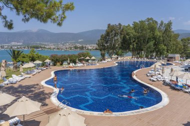 Didim, Türkiye - Eylül 02, 2019: İnsanlar Didim, Türkiye 'deki tatil otelinde denizin yanındaki havuzda yüzüyor ve güneşleniyor. Tatil ve eğlence kavramı