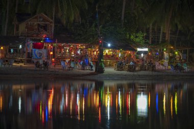 KOH PHANGAN, THAILAND - Mayıs 03, 2019: Sahil barı, hindistan cevizi palmiyesi ağaçları, deniz suyu ve gece kulübü, Tayland 'ın Koh Phangan adasındaki deniz suyuna yansımaktadır.