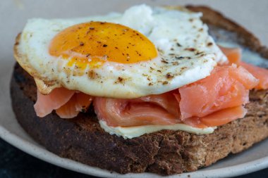 Taze somon, yumurtalı sandviç, yakın çekim. Tuzlu somon, sahanda yumurta, tereyağı ve tabakta siyah ekmek.