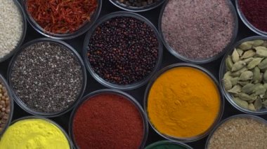 Arka planda farklı baharatlar ve bitkiler dönüyor, yakın plan, üst görünüm. Renkli baharatlar, tohumlar ve yemek pişirmek için bitkiler.