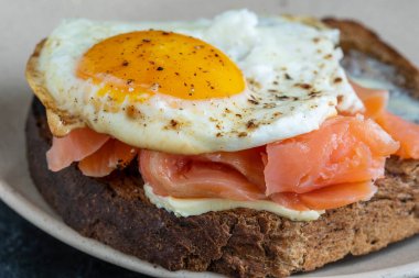 Taze somon, yumurtalı sandviç, yakın çekim. Tuzlu somon, sahanda yumurta, tereyağı ve tabakta siyah ekmek.