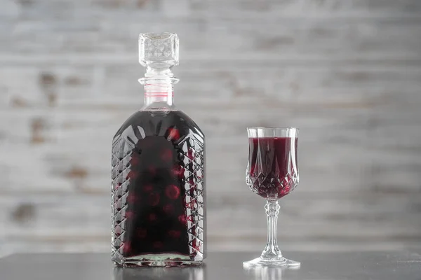 ガラス瓶の中の赤いチェリーの自家製チンキとグレーの背景にあるワインクリスタルガラス ウクライナ クローズアップ ベリーアルコール飲料のコンセプト — ストック写真