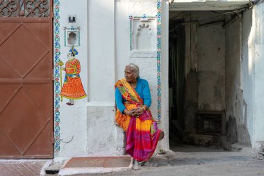 UDAIPUR, INDIA - 19 Kasım 2018: Yaşlı bir Hintli kadın Udaipur, Rajasthan, Hindistan 'daki evinin yanında oturuyor