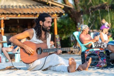 Koh Phangan, Tayland - 21 Ocak 2020: Tropikal ada Koh Phangan, Tayland 'da günbatımında plajda gitar çalan yakışıklı genç adam
