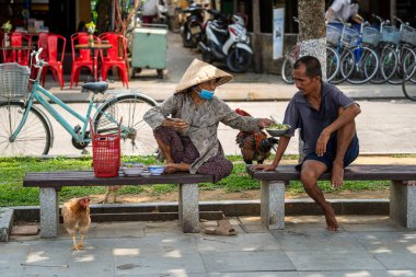 Hoi An, Vietnam - 16 Mart 2020: Vietnamlı yaşlı bir kadın ve erkek bir bankta oturur ve Hoi An, Vietnam 'daki eski bir şehirde yemek yer.
