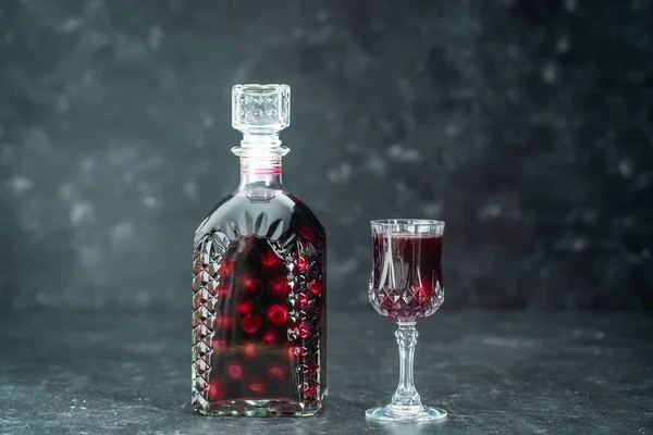 ガラス瓶の中の赤いチェリーの自家製チンキとグレーの背景にあるワインクリスタルガラス ウクライナ クローズアップ ベリーアルコール飲料のコンセプト — ストック写真