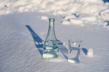 Kışın beyaz bir karda cam şişe ve bir bardak su yakın.