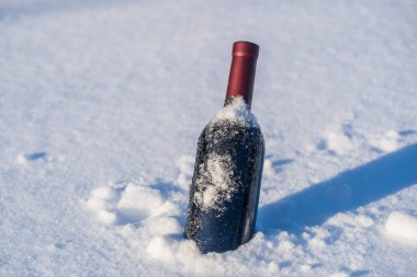 Kar yatağında bir şişe kırmızı şarap ve beyaz arka plan, yakın çekim.
