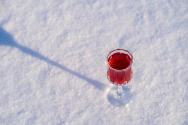 Ukrayna 'da, kar ve beyaz arka planda şarap kristal bardağında ev yapımı kırmızı kiraz tentürü. Böğürtlen alkollü içki konsepti