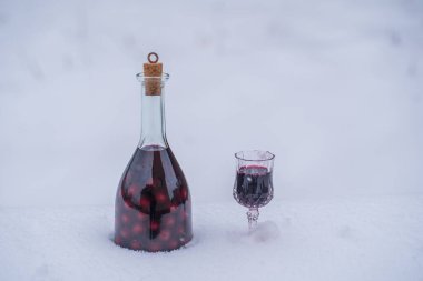 Cam bir şişede ev yapımı kırmızı kiraz tentürü ve kar ve beyaz arka planda şarap kristali, Ukrayna, yakın plan. Böğürtlen alkollü içki konsepti