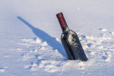 Kar yatağında bir şişe kırmızı şarap ve beyaz arka plan, yakın çekim.