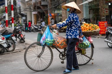 Hanoi, Vietnam - Mart 01, 2020: Bisikletli Vietnamlı kadın Hanoi, Vietnam 'da eski bir kasabanın sokak yiyecek pazarında taze meyve satıyor.