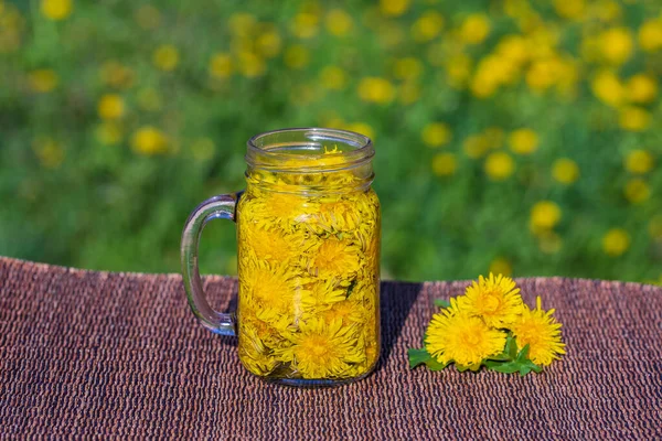 Dandelion yellow flower tea drink in glass mug on the table in nature background, outdoors, close up. Concept of healthy eating