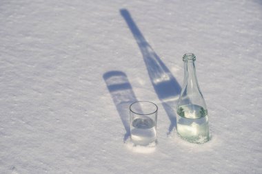 Kışın beyaz bir karda cam şişe ve bir bardak su yakın.