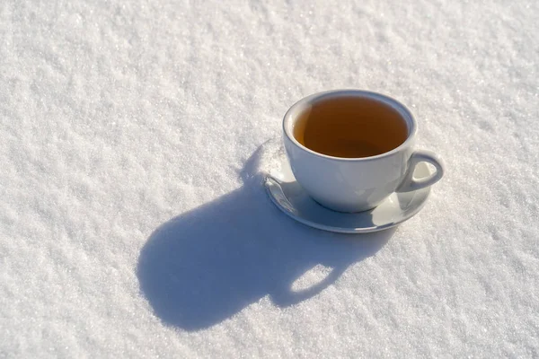 White cup of hot tea on a bed of snow and white background, close up. Concept of christmas winter morning