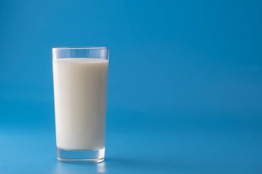 Mavi arka planda izole edilmiş beyaz süt bardağı, yakın plan. Süt ürünü konsepti, kopyalama alanı