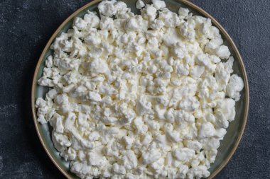 Arkadaki tabakta süzme peynir, üst manzara. Süt ürünlerinin beyaz taneli dokusu, süzme peynir, yakın çekim. Süt ürünü konsepti