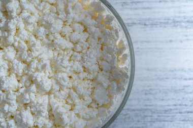 Arka planda cam kase içinde süzme peynir, üst manzara. Süt ürünlerinin beyaz taneli dokusu, süzme peynir, yakın çekim. Süt ürünü konsepti