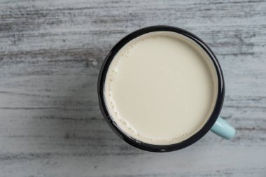 Beyaz ahşap arka planda metal bardakta beyaz süt, yakın plan, üst manzara. Süt ürünü konsepti, kopyalama alanı