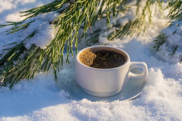 White cup of hot coffee on a bed of snow and white background, close up. Concept of christmas winter morning