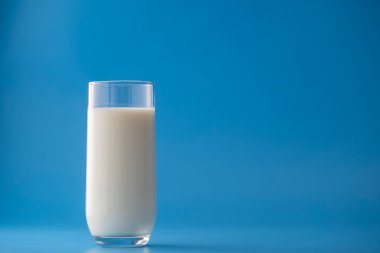 Mavi arka planda izole edilmiş beyaz süt bardağı, yakın plan. Süt ürünü konsepti, kopyalama alanı