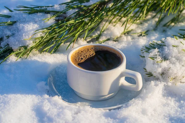 White cup of hot coffee on a bed of snow and white background, close up. Concept of christmas winter morning