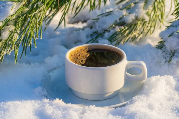 White cup of hot coffee on a bed of snow and white background, close up. Concept of christmas winter morning