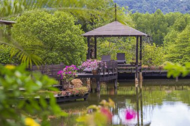 Terasta dinlenmek için güneşli odunları olan ahşap bir çardak. Tayland 'daki tropik bir adanın yanındaki gölün yanında çiçekler. Doğa ve seyahat kavramı