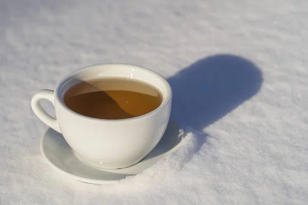 White cup of hot tea on a bed of snow and white background, close up. Concept of christmas winter morning