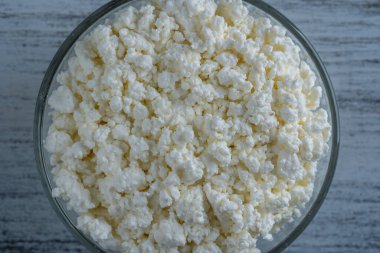 Arka planda cam kase içinde süzme peynir, üst manzara. Süt ürünlerinin beyaz taneli dokusu, süzme peynir, yakın çekim. Süt ürünü konsepti