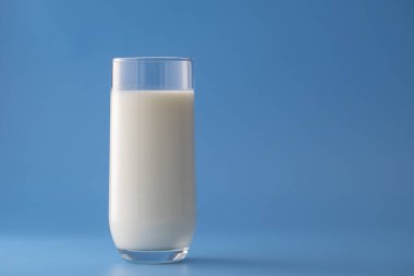 Mavi arka planda izole edilmiş beyaz süt bardağı, yakın plan. Süt ürünü konsepti, kopyalama alanı