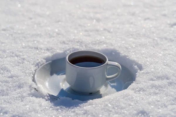 White cup of hot coffee on a bed of snow and white background, close up. Concept of christmas winter morning