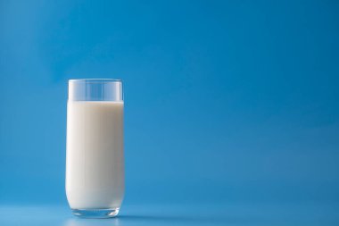 Mavi arka planda izole edilmiş beyaz süt bardağı, yakın plan. Süt ürünü konsepti, kopyalama alanı