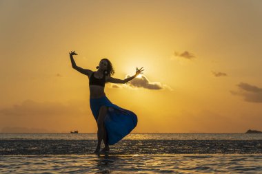 Gün batımında, Tayland 'daki cennet adasında tropikal sahilde dans eden genç bir kız. Yaz kavramı. Tatil seyahati.