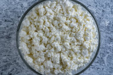 Arka planda cam kase içinde süzme peynir, üst manzara. Süt ürünlerinin beyaz taneli dokusu, süzme peynir, yakın çekim. Süt ürünü konsepti