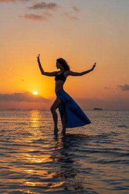 Gün batımında, Tayland 'daki cennet adasında tropikal sahilde dans eden genç bir kız. Yaz kavramı. Tatil seyahati.