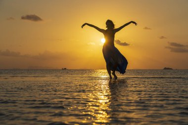 Gün batımında, Tayland 'daki cennet adasında tropikal sahilde dans eden genç bir kız. Yaz kavramı. Tatil seyahati.